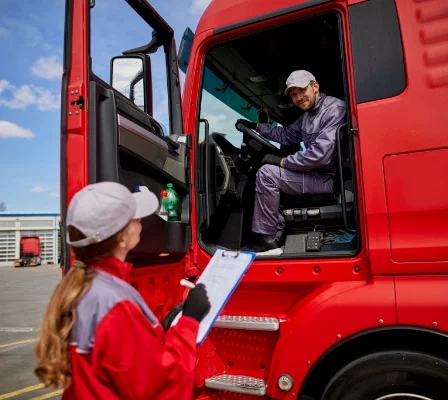 Kobieta trzymająca dokument rozmawiający z mężczyzną siedzącym w kabinie pojazdu ciężarowego